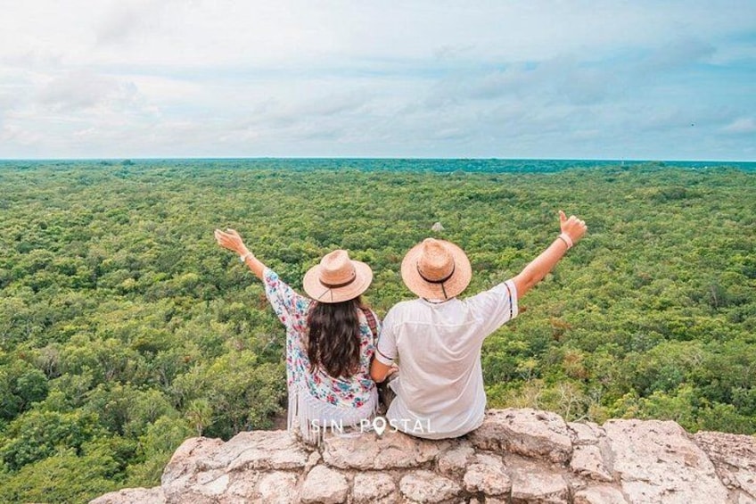 Two people sitting on a stone ledge overlooking a dense forest. 3
