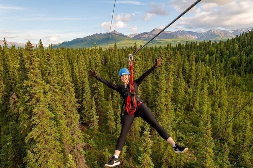 A person ziplining through a forest with mountains in the background. 1