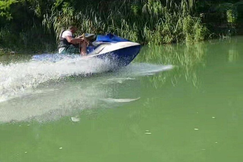 A person jet-skiing on a green body of water with dense vegetation in the background. 3