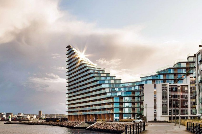 A modern building with a unique curved design, a waterfront location, and a clear sky. 4