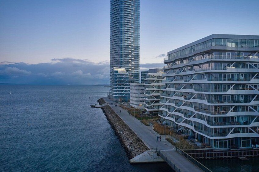 A coastal cityscape with modern high-rise buildings, a waterfront promenade, and a clear sky. 5