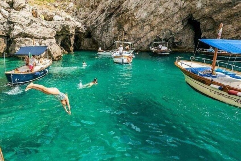Mar azul cristalina con barcos, una pared rocosa de cueva y gente nadando. 4