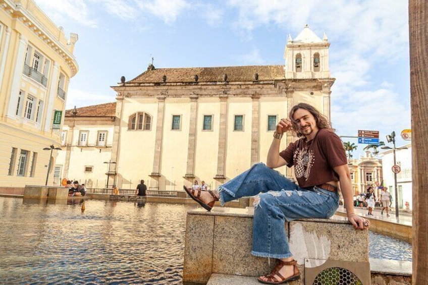 Una persona sentada en un muro de piedra junto a un canal, con edificios y una torre al fondo. 4