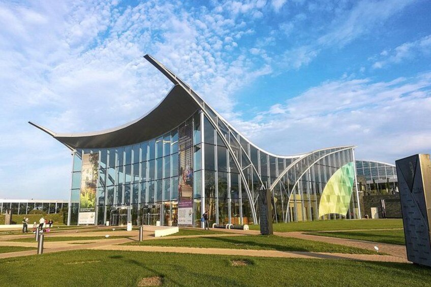 A modern glass building with a curved roof and a green sculpture in front. 3
