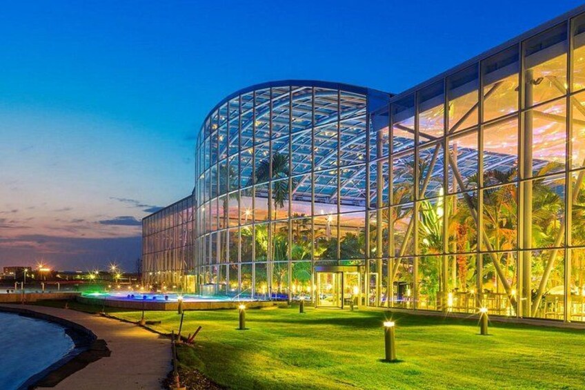 A modern glass building with a curved facade, surrounded by a well-lit grassy area and a body of water. 4
