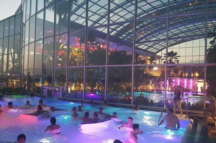 An indoor swimming pool with people swimming, surrounded by a glass building with a transparent roof. 5