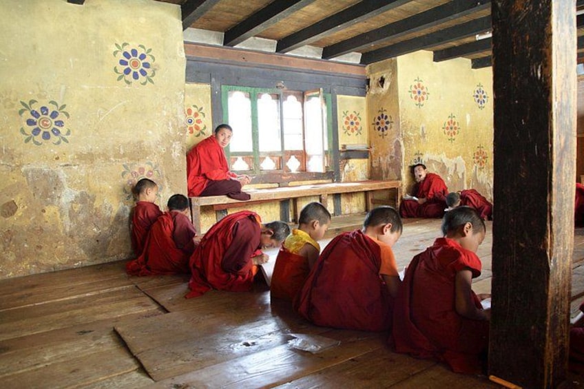 Monks in red robes seated on wooden floors in a room with traditional decor. 2