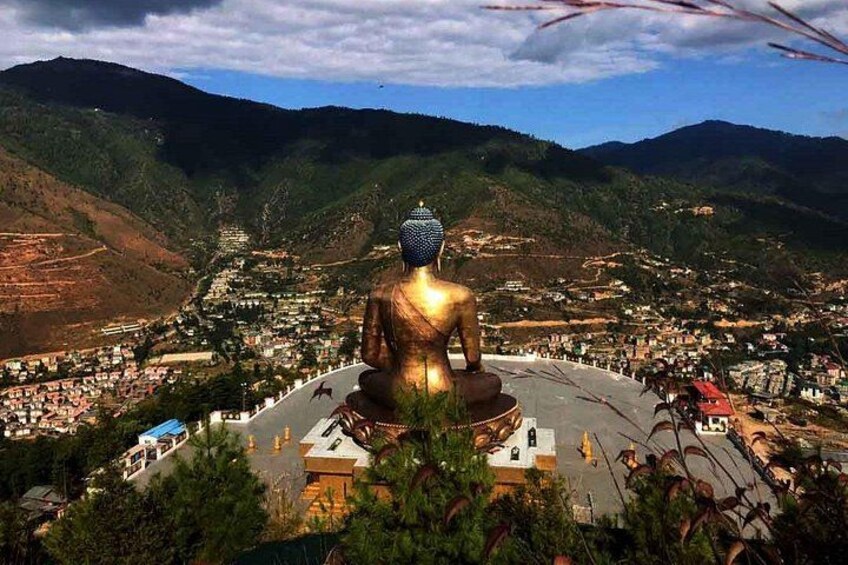 A large golden statue of Buddha surrounded by a circular structure, set against a mountainous landscape with a town below. 3