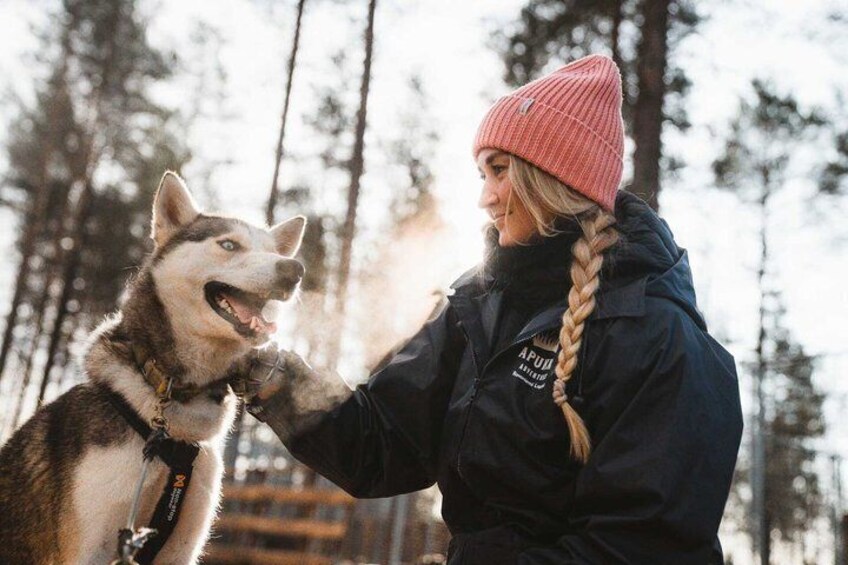 A person with a braided hairstyle petting a husky dog in a forested area. 3