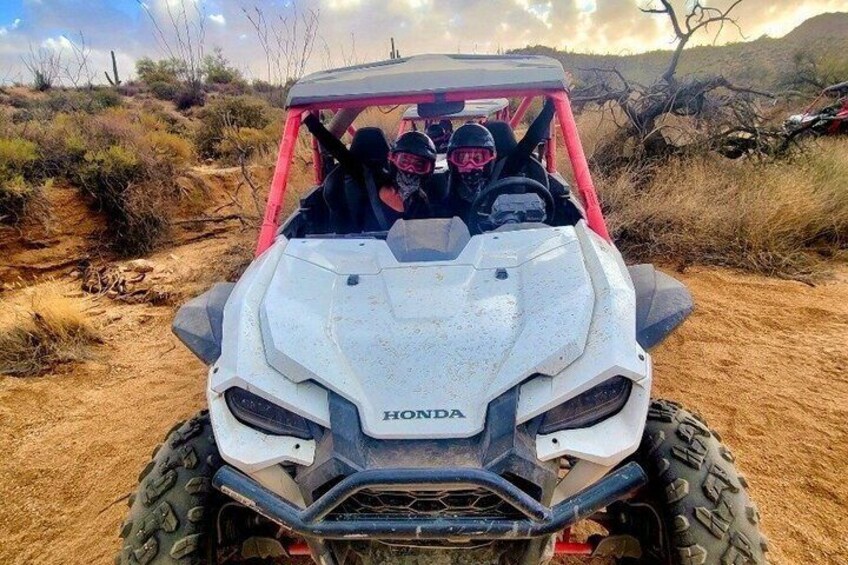 A white Honda ATV with two people in the back, a red frame, and a desert landscape with sparse vegetation. 4
