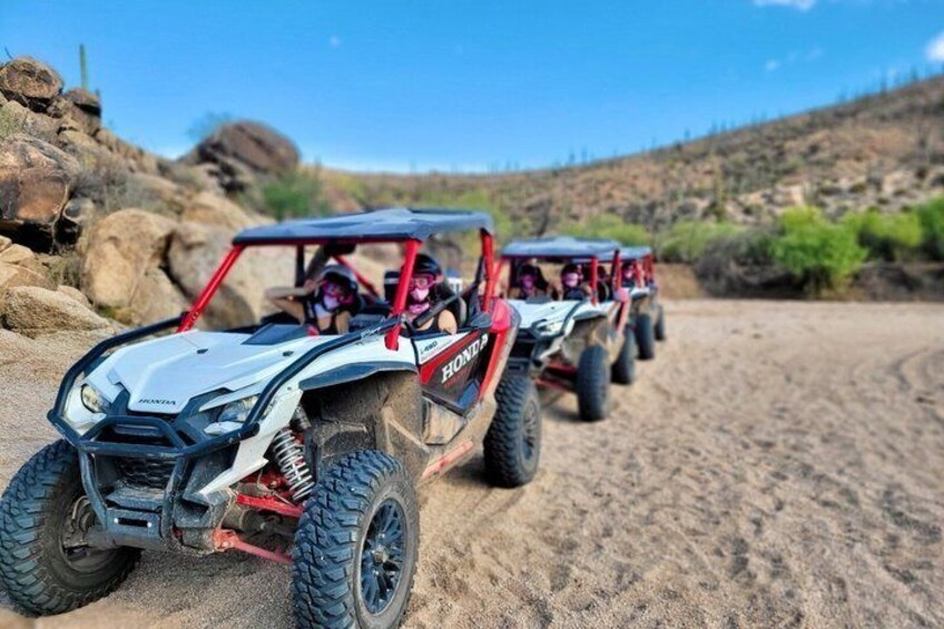 A white and red off-road vehicle with a driver, on a sandy terrain with rocks and sparse vegetation. 3