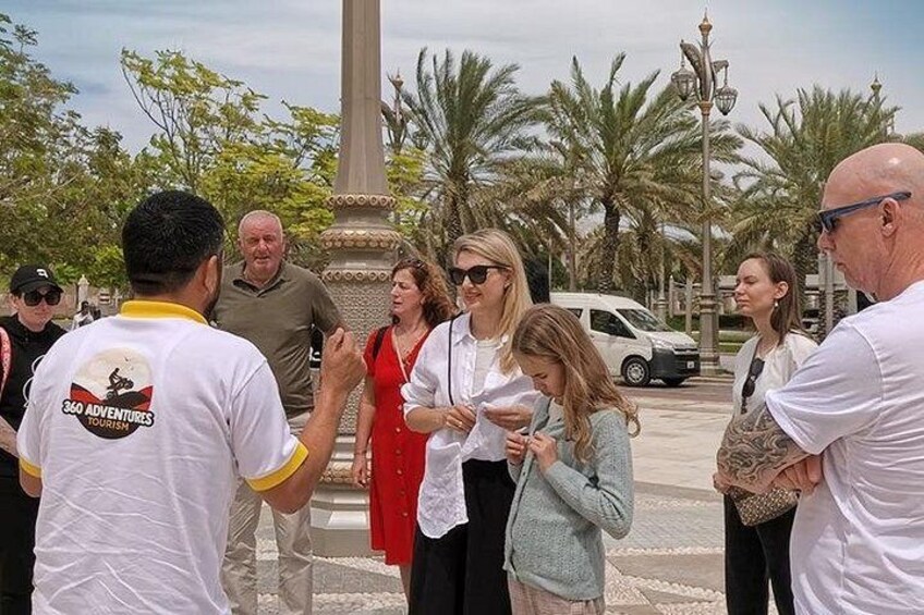 A group of people standing outdoors near a monument, with palm trees and a street lamp in the background. 4