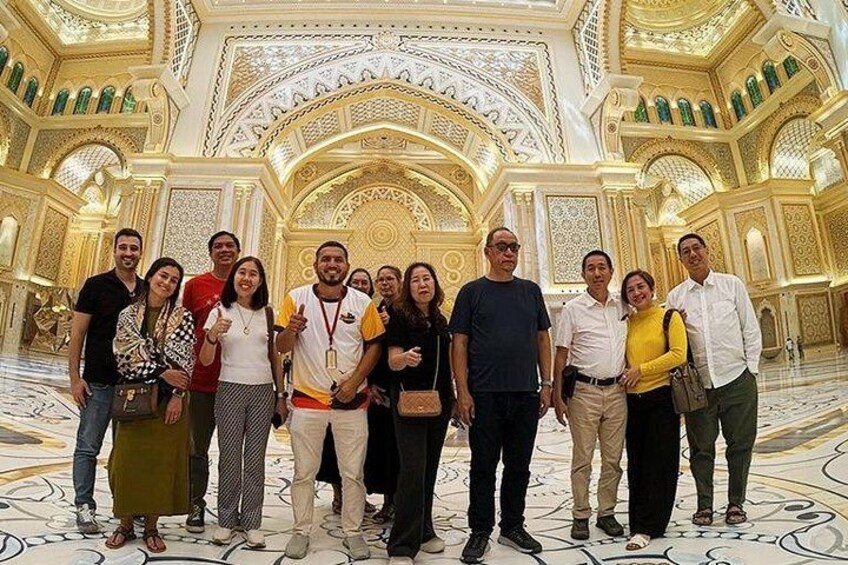 A group of people in a grand, ornately decorated interior space with intricate ceiling designs and patterned flooring. 3