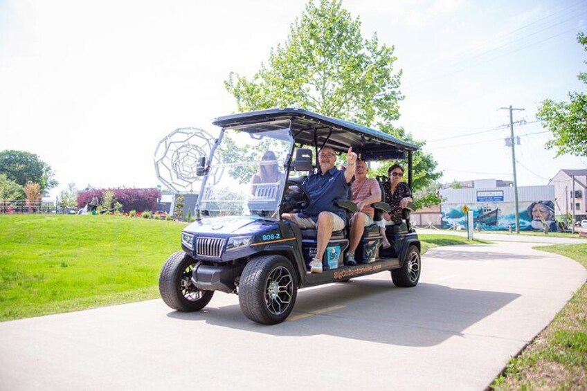A golf cart with four passengers on a paved path. 3