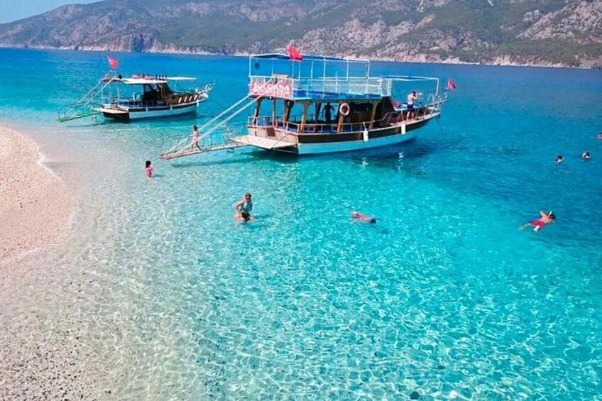 Una playa con agua turquesa cristalina, barcos y gente nadando. 2