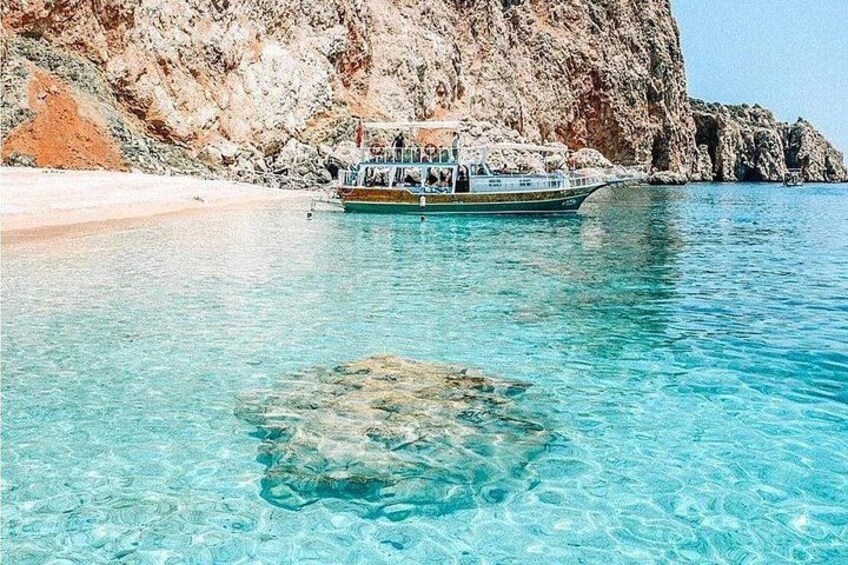 Un bote en un mar turquesa y transparente, con un acantilado rocoso al fondo. 4