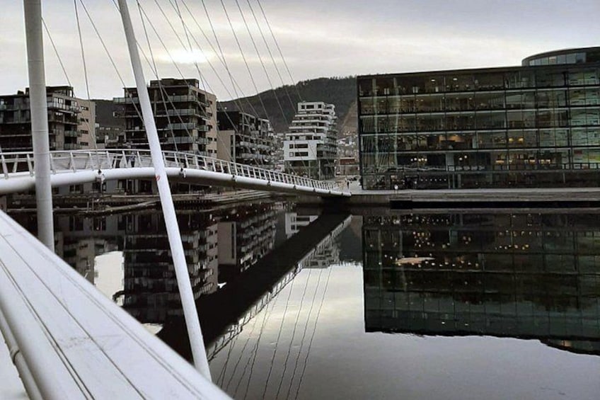 Een moderne brug met een glazen gevel die gebouwen en een bergachtige achtergrond weerspiegelt. 4