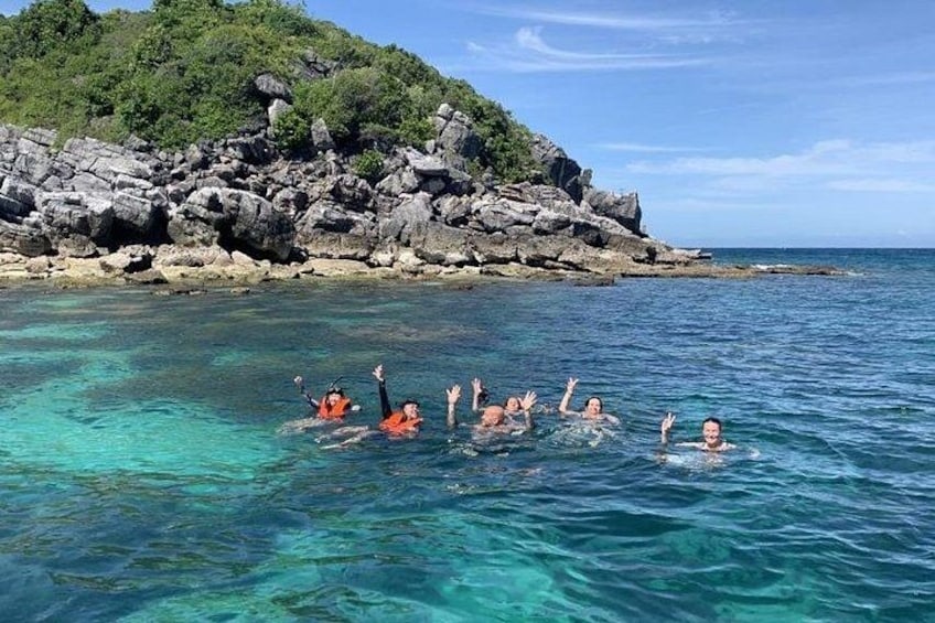 People swimming in clear blue water with a rocky coastline in the background. 5