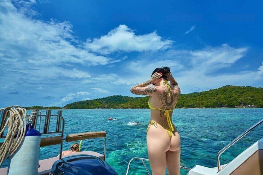 A person in a yellow bikini on a boat with clear blue water and a forested island in the background. 4