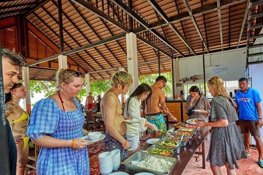 People at a buffet under a covered area with food and drinks. 2