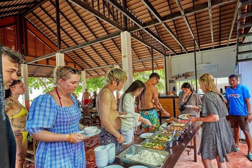 A group of people dining at an outdoor buffet with various food items and a covered structure. 2