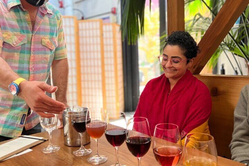 A person pouring a drink into a glass at a table with several other glasses. 1