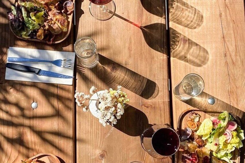 A wooden table with a salad, wine glasses, and a plate of food. 3