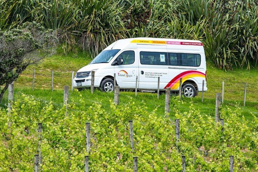 A white van with colorful graphics parked in a field with a fence and greenery in the background. 3
