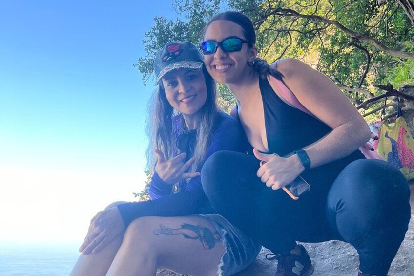 Dos personas sentadas sobre una roca junto al mar, una sosteniendo un teléfono. 2