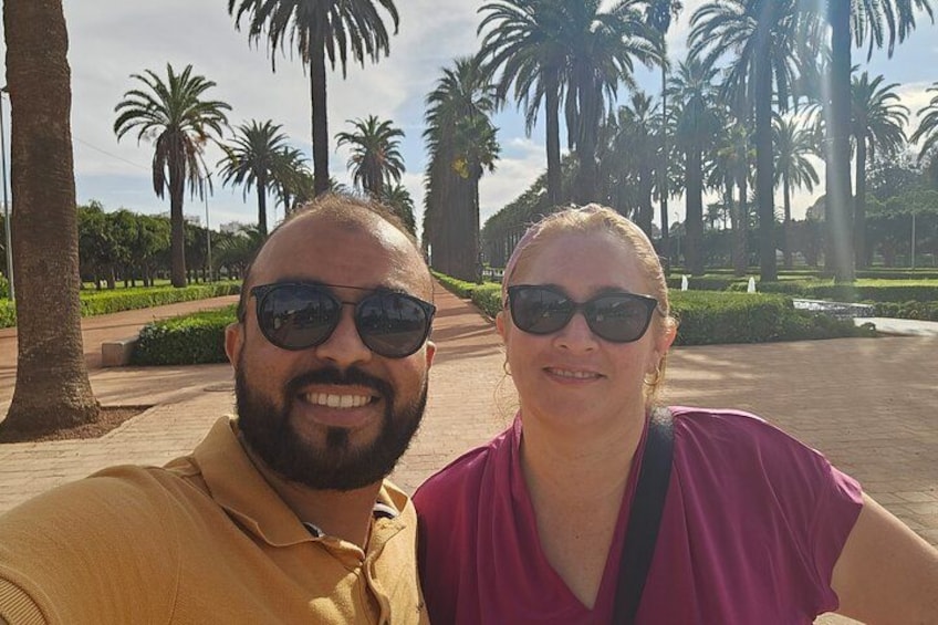 Two people taking a selfie in a park with palm trees and a paved walkway. 3