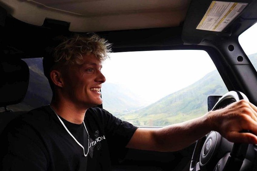 A person driving a vehicle with a mountainous landscape in the background. 2