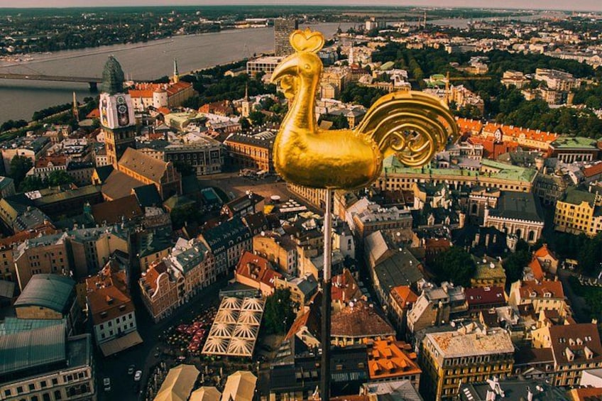 Una escultura de gallo dorado en un paisaje urbano con edificios y un río. 5