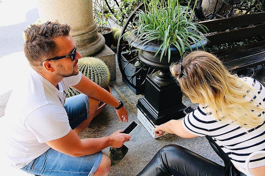 Dos personas sentadas en el suelo, una sosteniendo un teléfono inteligente, y una planta en maceta al fondo. 3