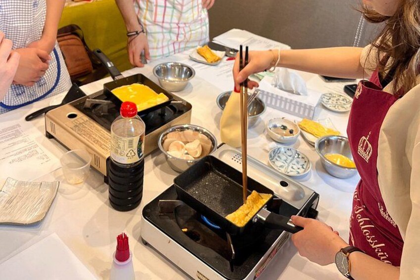 A person cooking with a pan, chopsticks, and various bowls on a table. 2