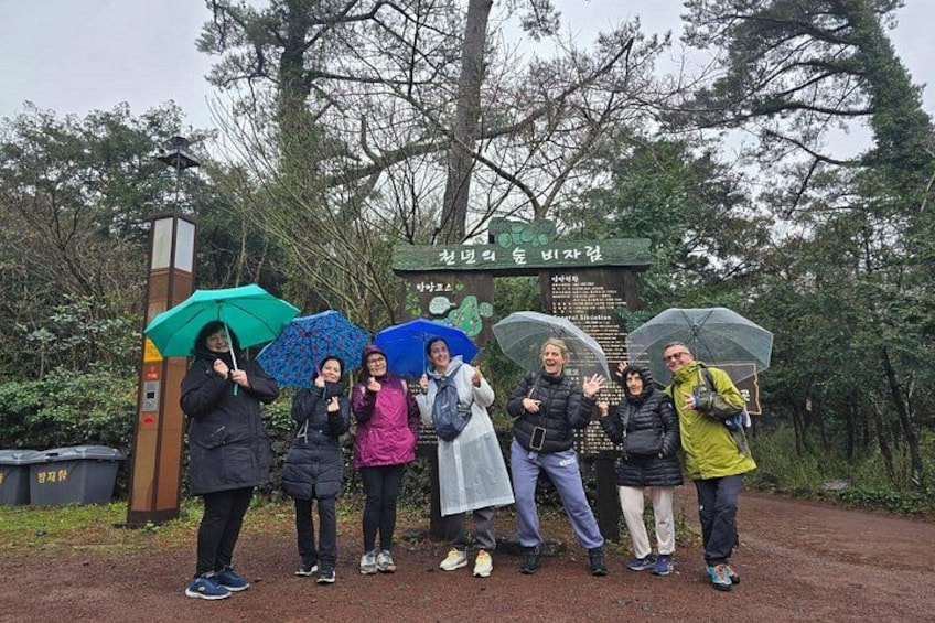 A group of people standing in a forested area with a sign in the background. 3