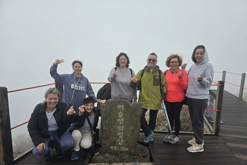 A group of people posing on a wooden platform with a stone monument in the foreground. 5