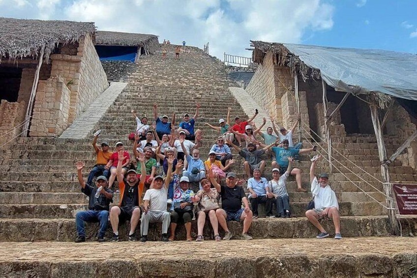 Un groupe de personnes se trouve sur un escalier en pierre, et au sommet, on aperçoit des constructions aux toits de chaume. 3