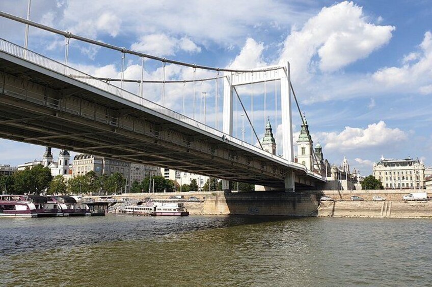 A bridge spanning a river with boats, buildings, and a clear sky. 2