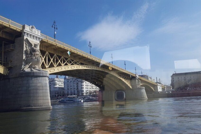 Een stenen brug met een standbeeld aan de linkerkant, over een rivier met gebouwen op de achtergrond. 2