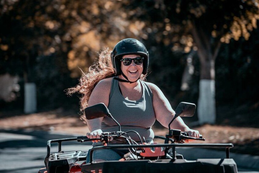 A person riding a quad bike on a paved path surrounded by trees. 1