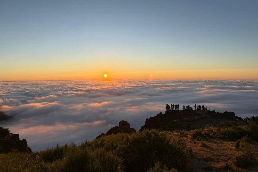 A sunrise over a cloud-covered landscape with a group of people on a hill. 3