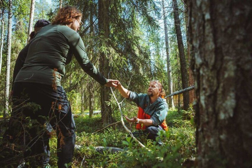 Two people in a forest, one standing and one crouching, holding a stick. 2