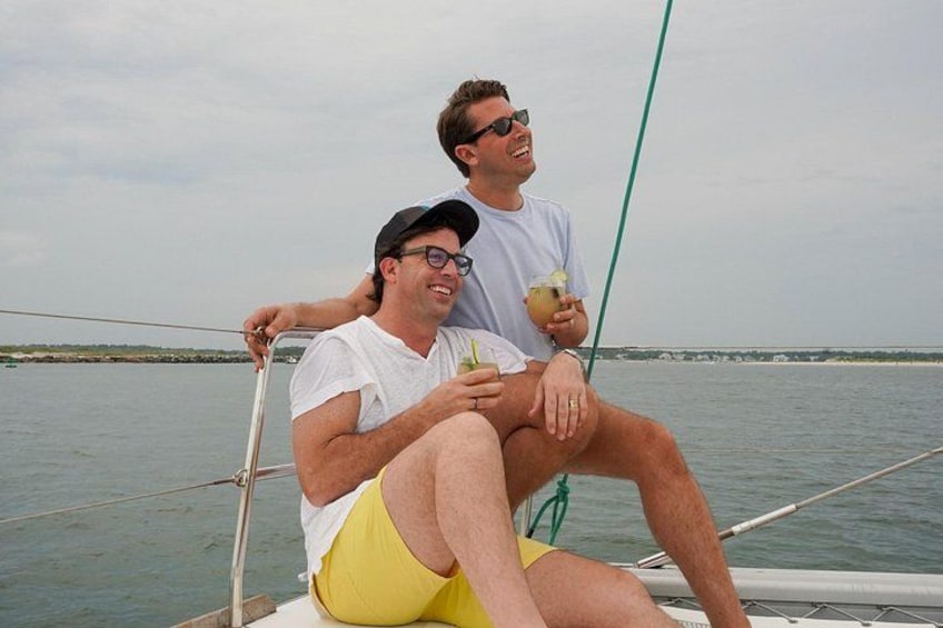 Two people on a boat, one holding a drink, with water and a distant shoreline in the background. 3