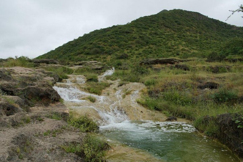 Ein kleiner Wasserfall in einer grünen Landschaft mit einer Hügelkette im Hintergrund. 5