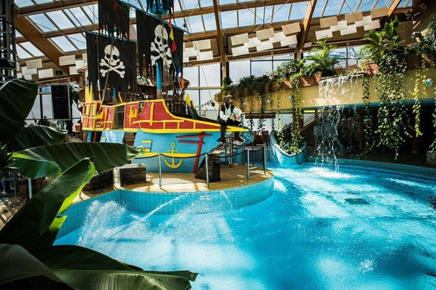 An indoor water park with a pirate-themed play area, a large pool, and waterfalls. 3