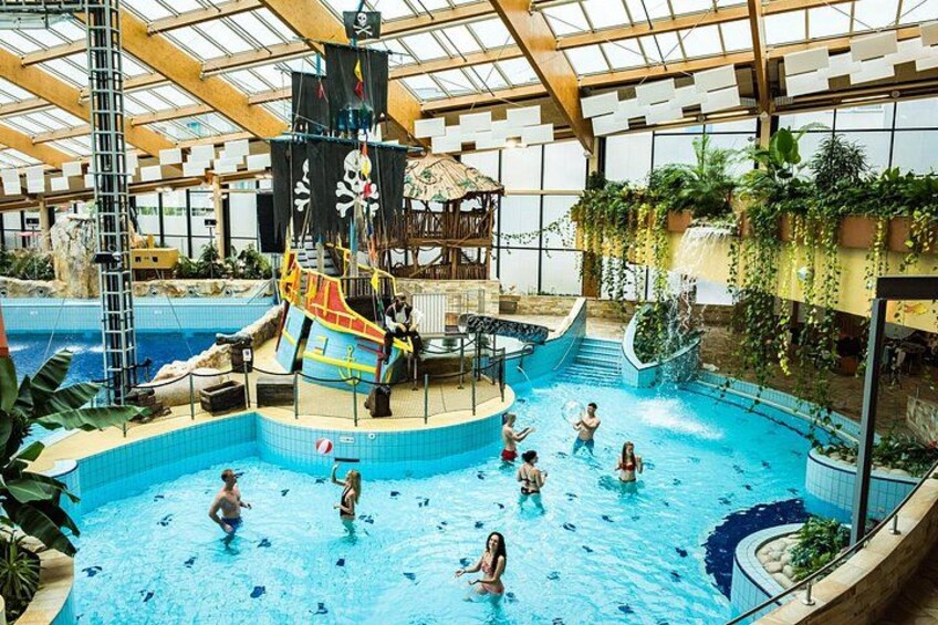 An indoor swimming pool with a pirate ship play area and a waterfall feature. 5