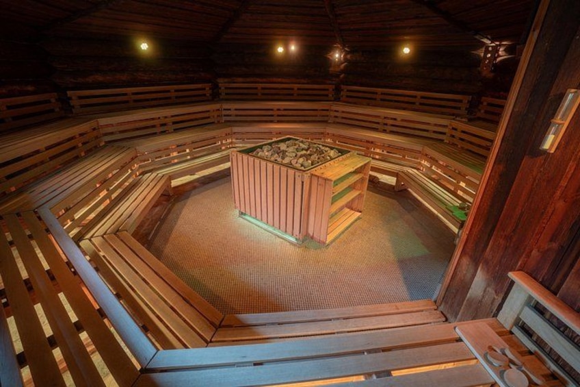 A wooden sauna with benches arranged in a semi-circle around a central heated stone. 2