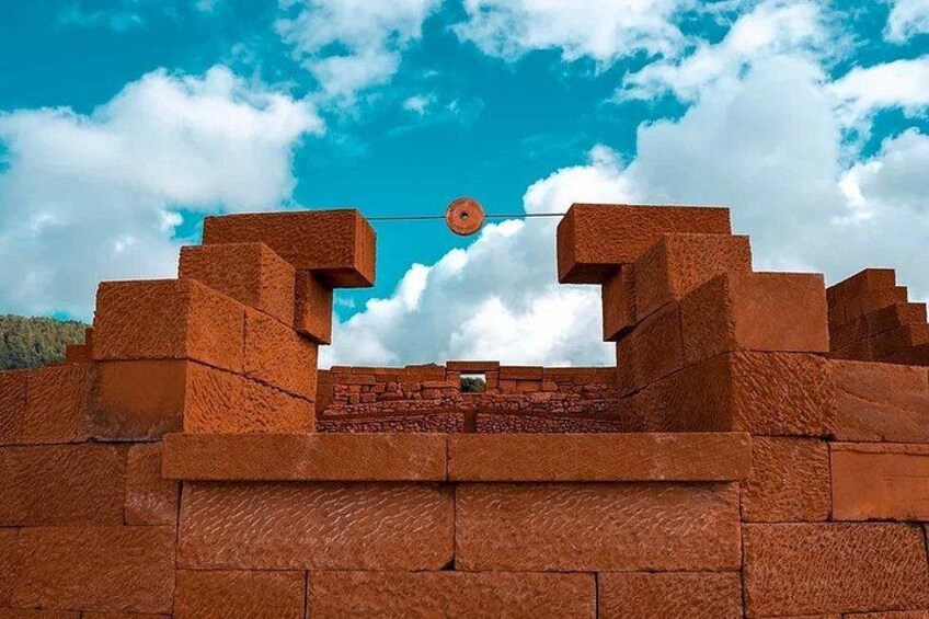 A brick structure with a circular opening at the top, set against a blue sky with clouds. 2