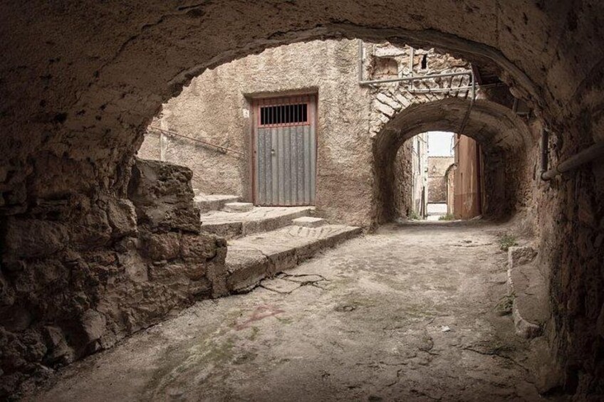 An arched stone passageway with a metal door and steps leading to a building. 4