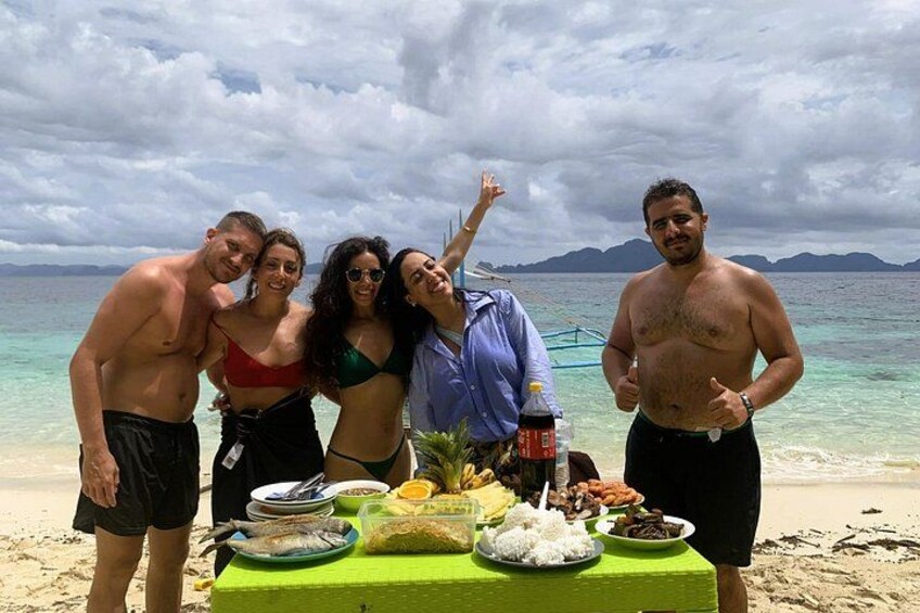 A group of people on a beach with a table of food and drinks. 2